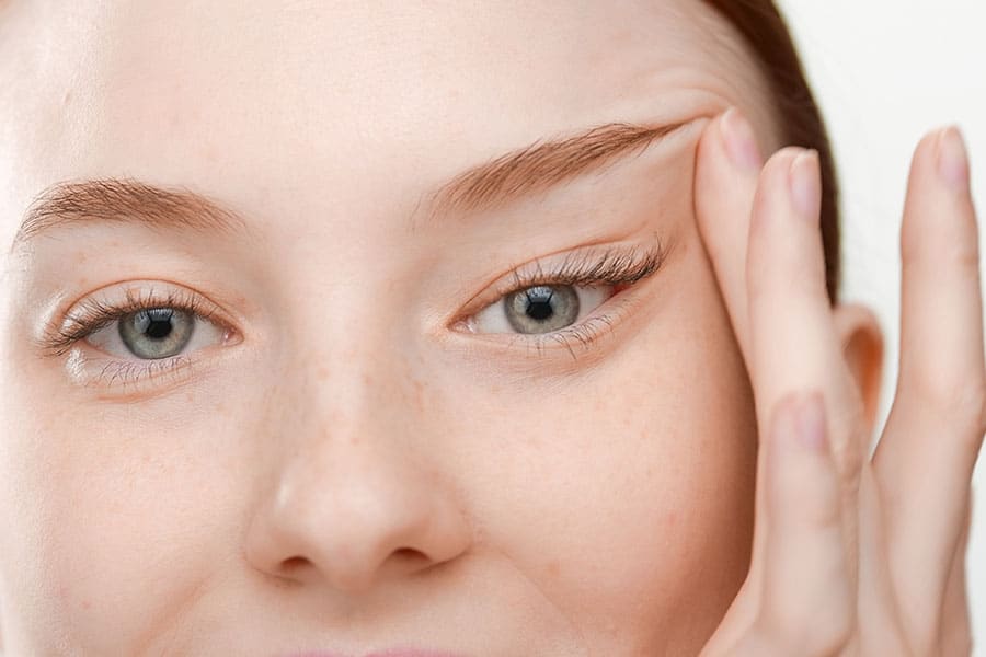 Extreme close-up shot of good-looking red haired female skin care model lifts her eyes