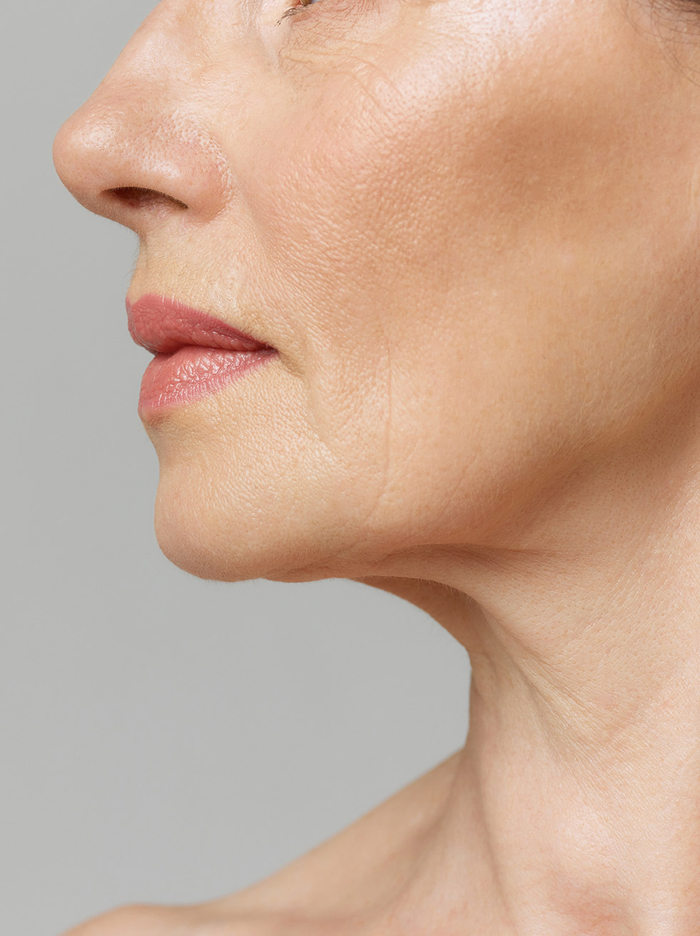 Cropped profile portrait with lips and chin neckline of middle-aged woman over grey studio background.